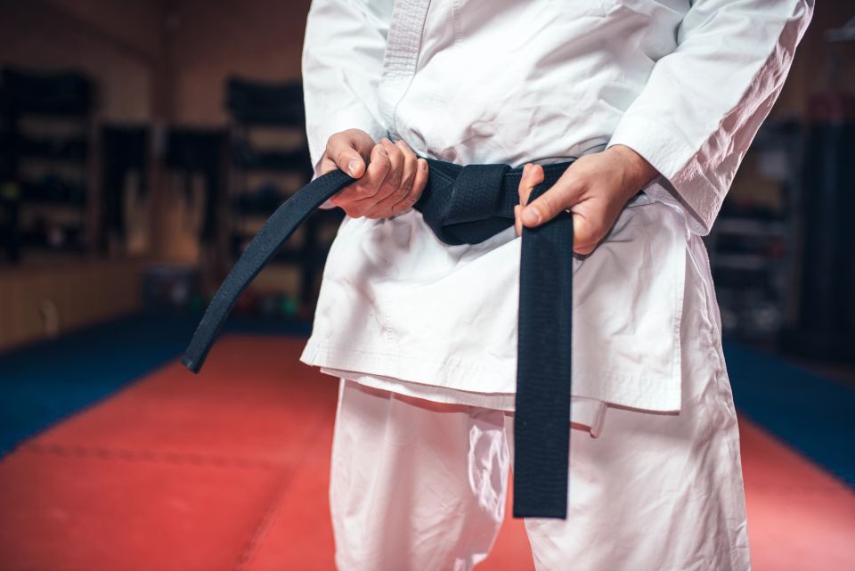 A karate sensei adjusting his black belt around his waist in a dojo.