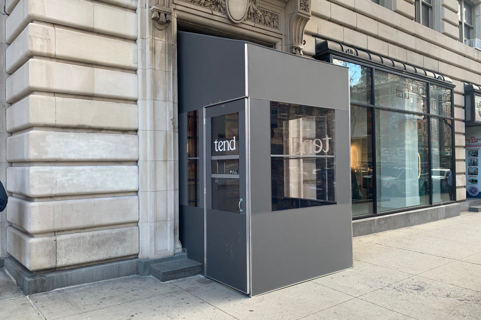 Grey aluminum framed vestibule with clear panels and white vinyl door lettering at the entrance of a limestone building