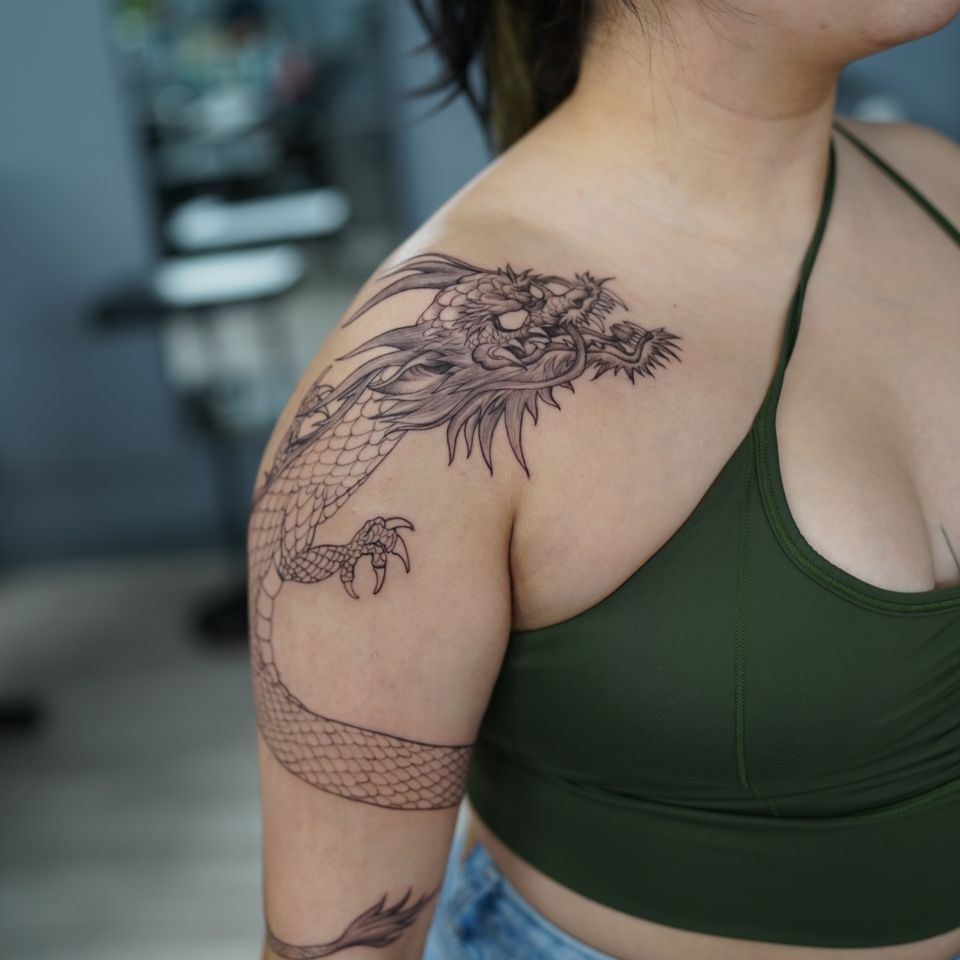 Image of a large angry dragon on a womans shoulder and wrapping around her arm down to her elbow