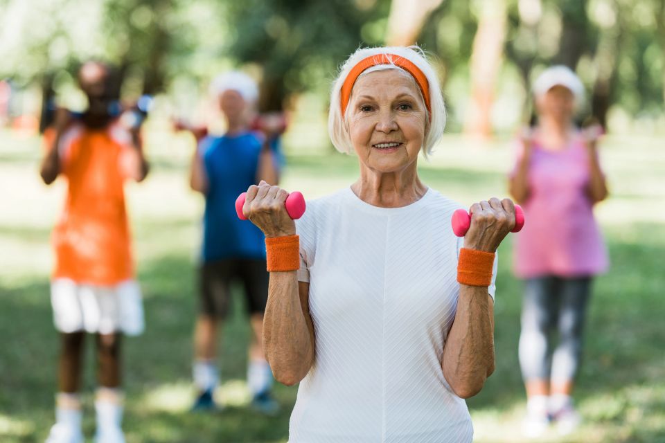 Senior woman lifting light dumbbells with a group during outdoor senior fitness training