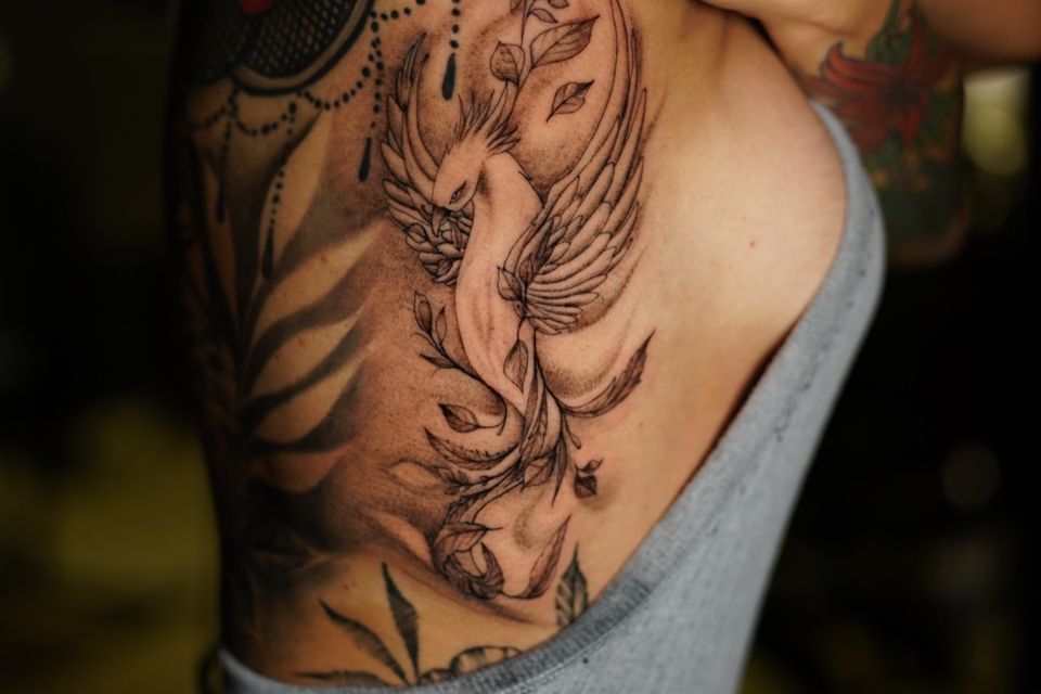Image of a large tattoo on the side and back of a woman of a Phoenix and plant leaves