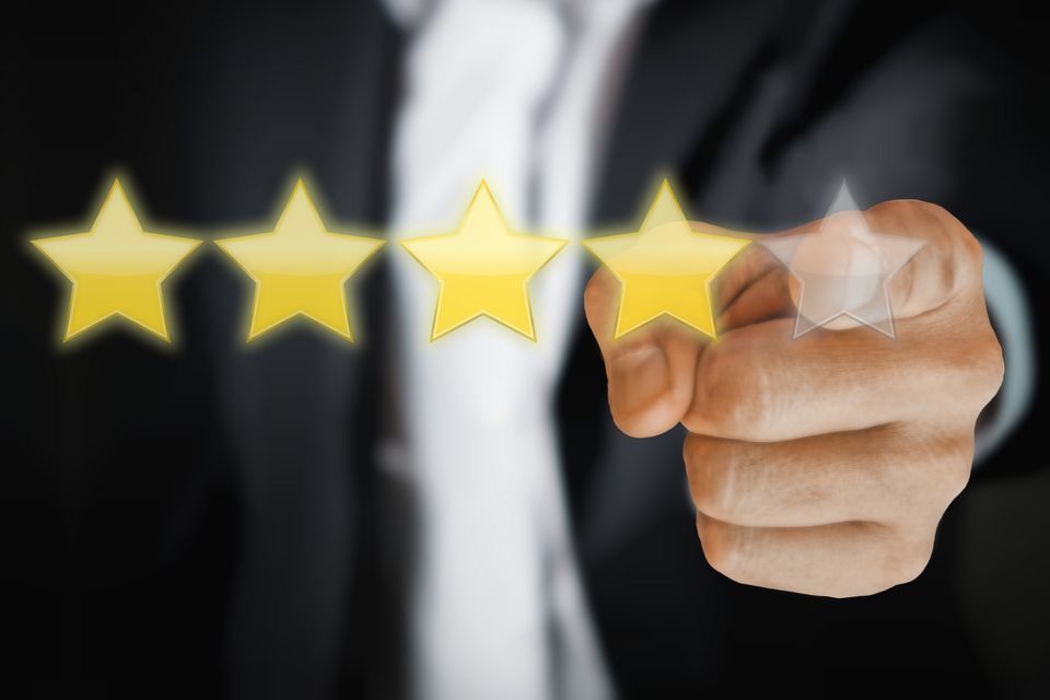 4 stars are light up in front of a person. There is a fifth star that's not lit up. Blurred in the background, a man wearing a suit points at the fifth star