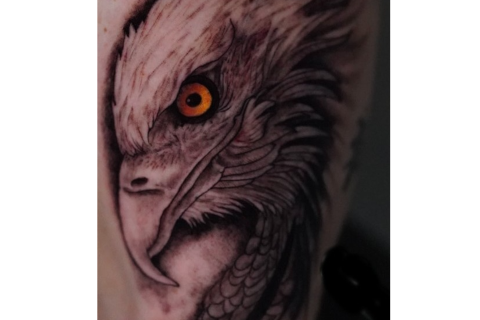 Image of an eagle tattoo in black and grey except the eye id golden with a mesmerizing black pupil