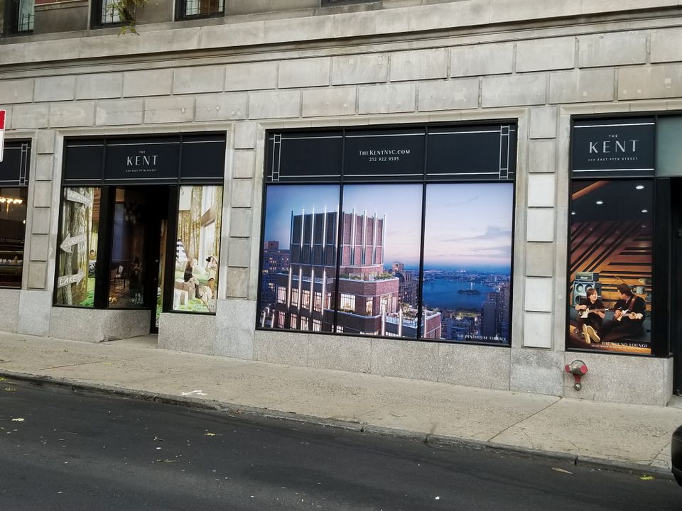 Printed window graphics filling four adjoining storefront windows along a stone building frontage