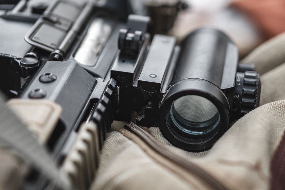 Close view of a magnified optic mounted on a black rifle receiver