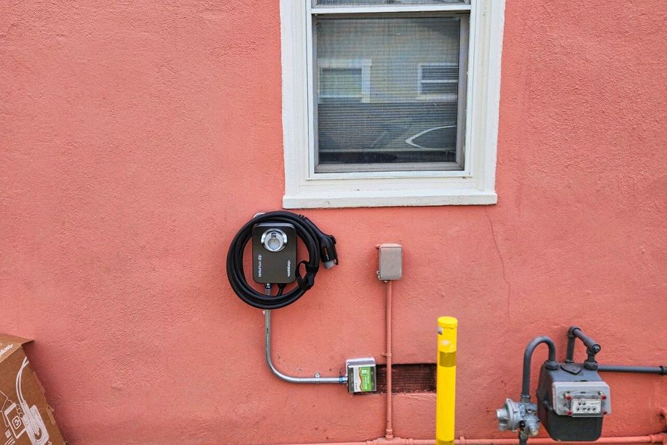 A wall-mounted Level 2 EV charging station with professionally installed metal conduit on a coral-colored stucco exterior next to a window
