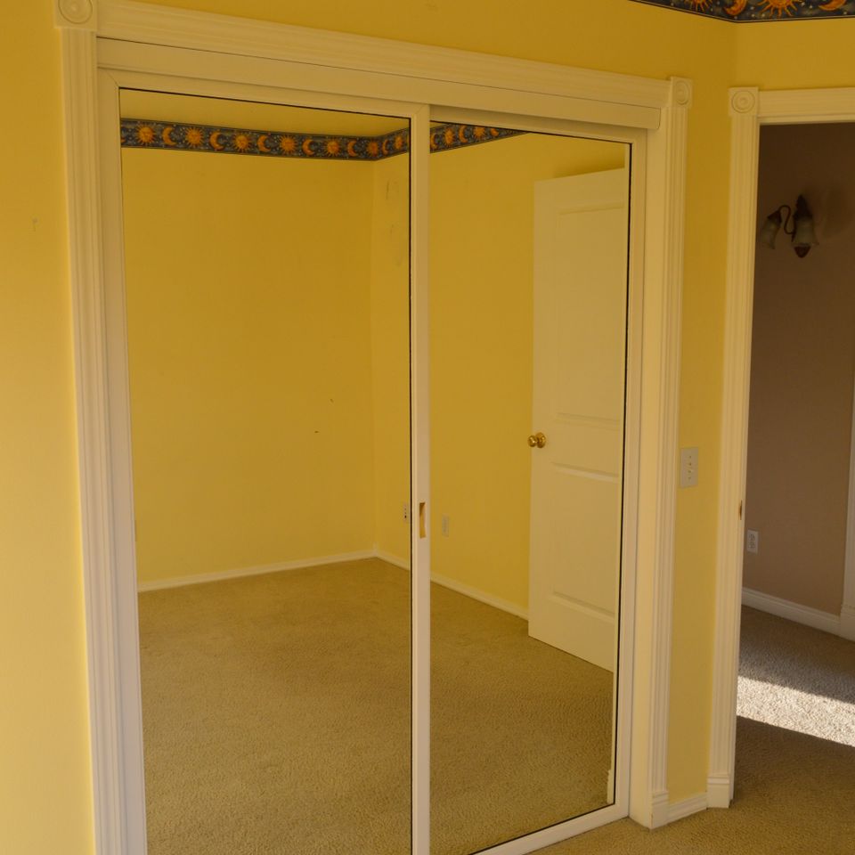 Bedroom with mirrored bypass closet doors and yellow walls in a finished custom home