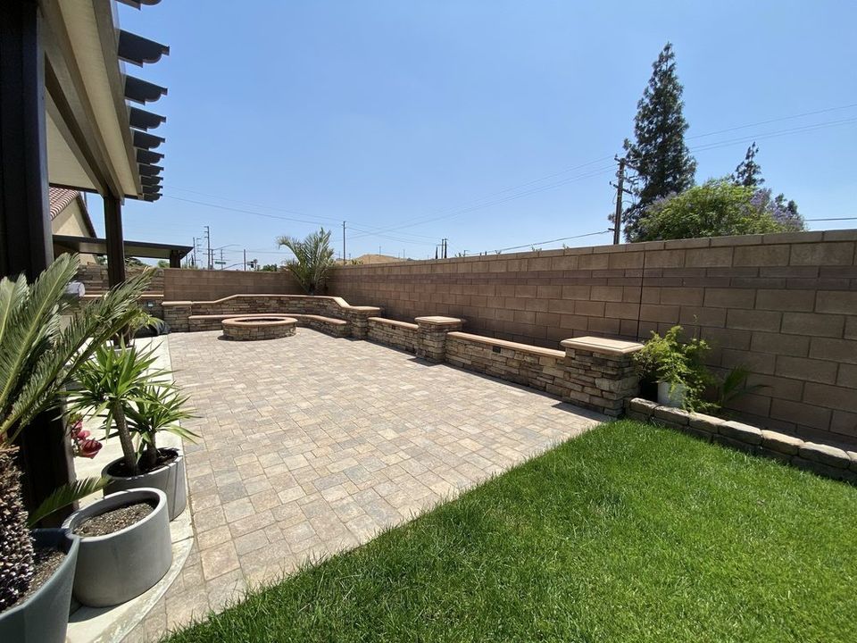 Custom backyard paver patio with raised seating wall, fire pit area, and landscaped lawn