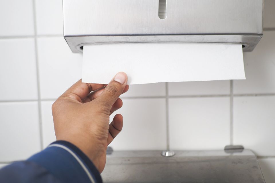 A mans hand taking a paper towel from the dispenser in a restroom
