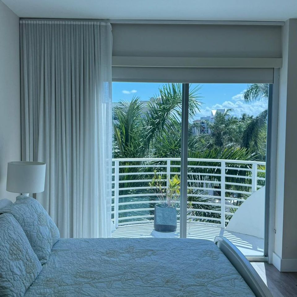 Sheer white drapes in a bright bedroom with sliding doors and a view of palm trees