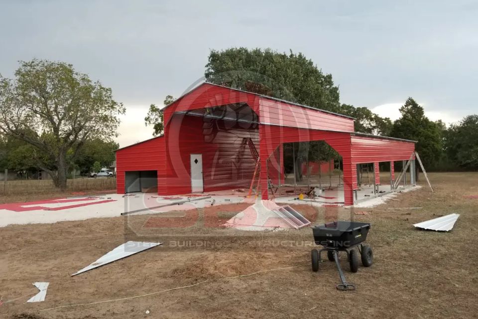Red steel barn with raised center roof under construction on rural lot with SBSI watermark representing steel barns in Alabama