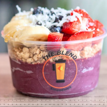 Acai bowl topped with strawberries, bananas, granola, and coconut in a branded cup 