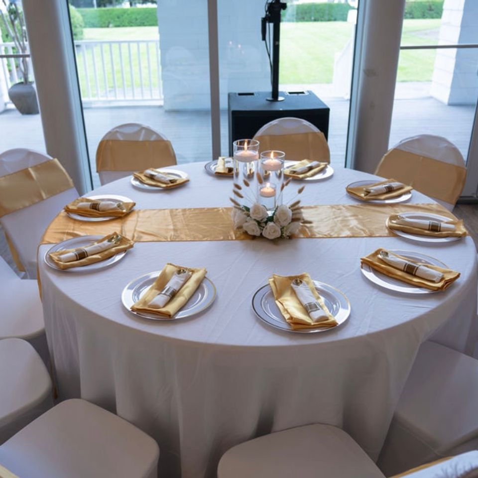 Round banquet table styled with gold sashes, satin napkins, and floating candle centerpiece