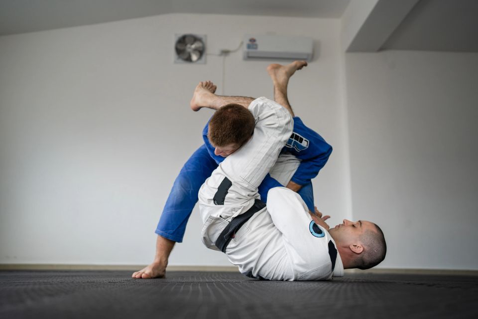 Two students in white and blue gis working guard position on the mat during Brazilian Jiu Jitsu class