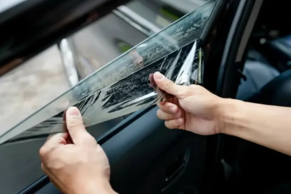 Professional technician carefully applying window tint film to a car door glass to ensure a bubble-free, custom fit.