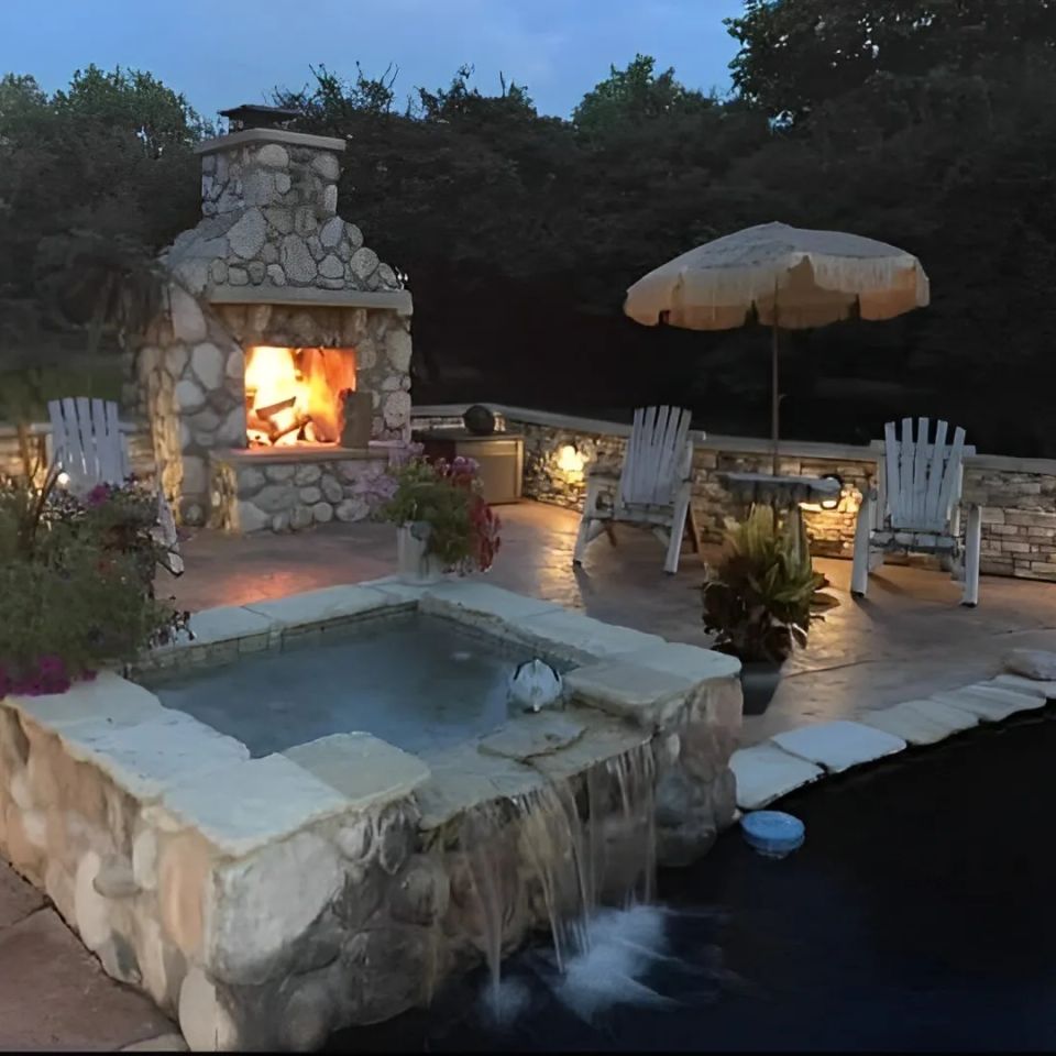 : Outdoor pool area with veneer stone fireplace, stone walls, and water features.