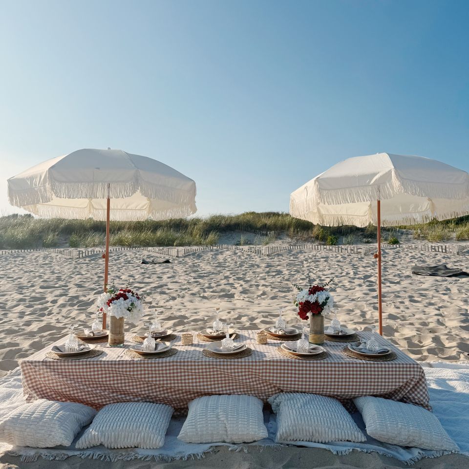 Two fringed umbrellas over a gingham beach picnic table set for eight in the Hamptons NY