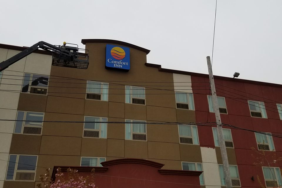 Illuminated square cabinet sign mounted high on a hotel facade with a boom lift alongside