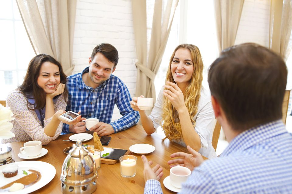 Group of four happy friends meeting and talking and eating