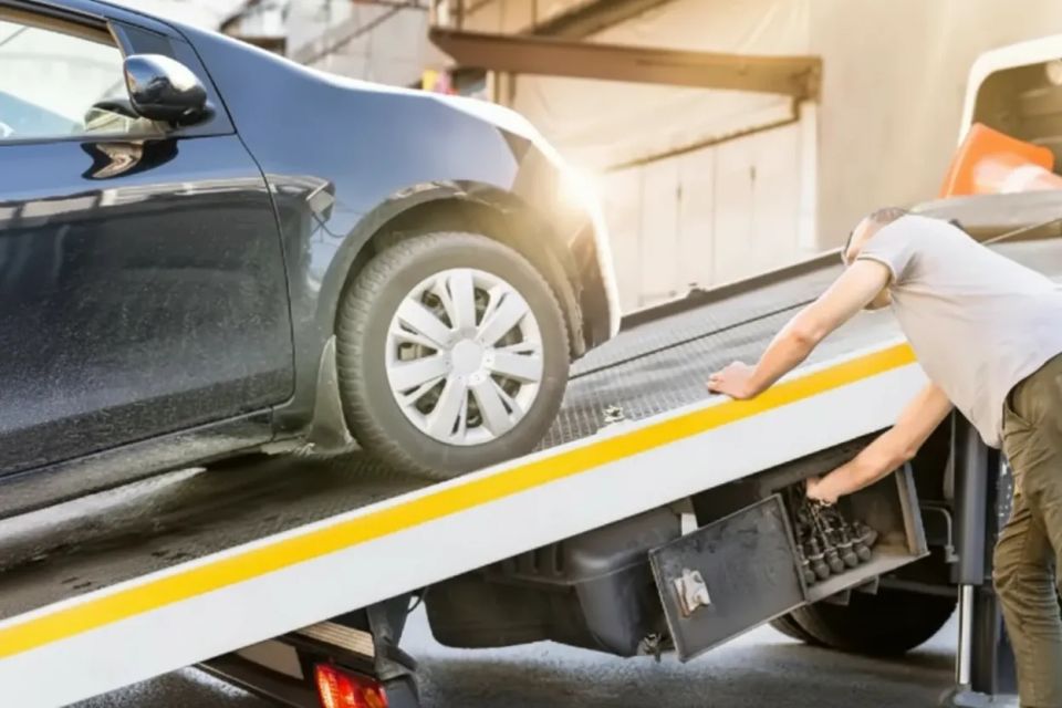 Tow truck operator safely winching a disabled sedan onto a flatbed truck for transport to a repair shop.