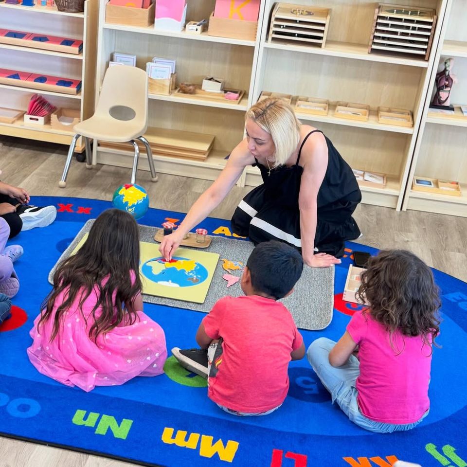 Teacher guiding preschool children with a world map puzzle during Montessori circle time in Palmdale CA