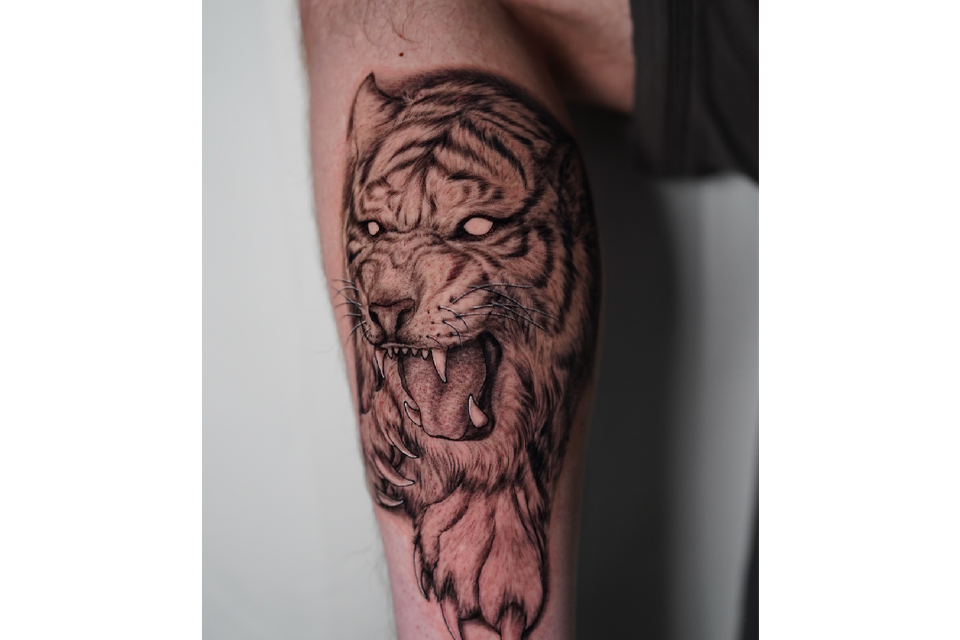 Image of a Tiger with no eyes on left calf of a man