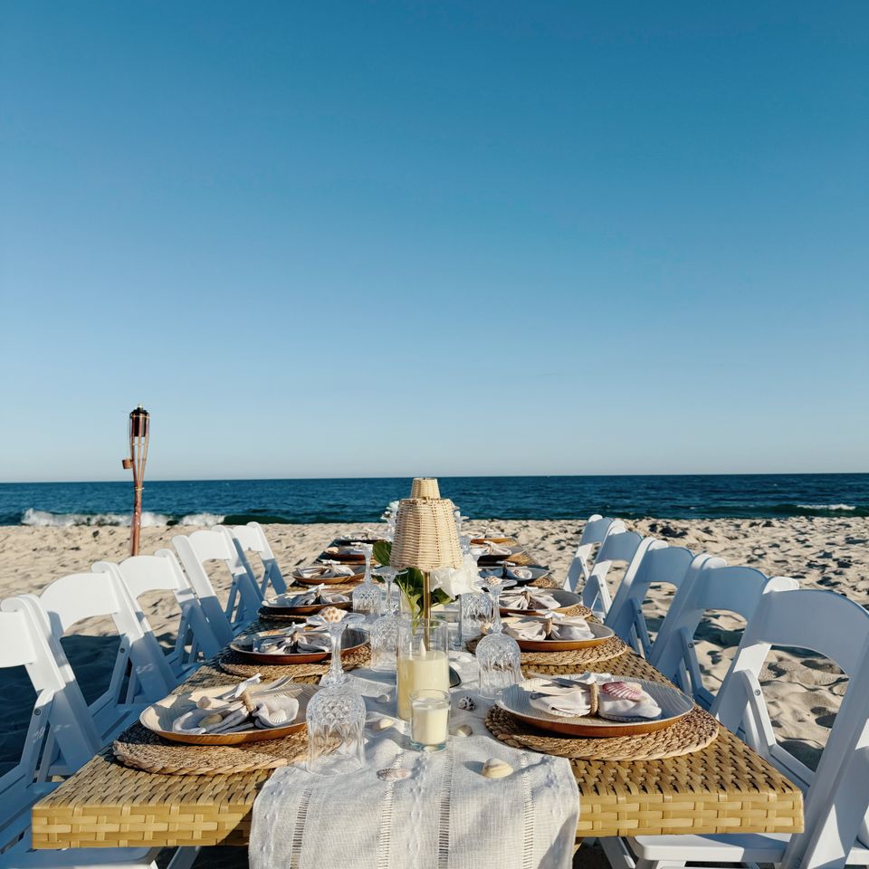 Coastal beach table styling with woven placemats, shells, and candles beside the water in the Hamptons