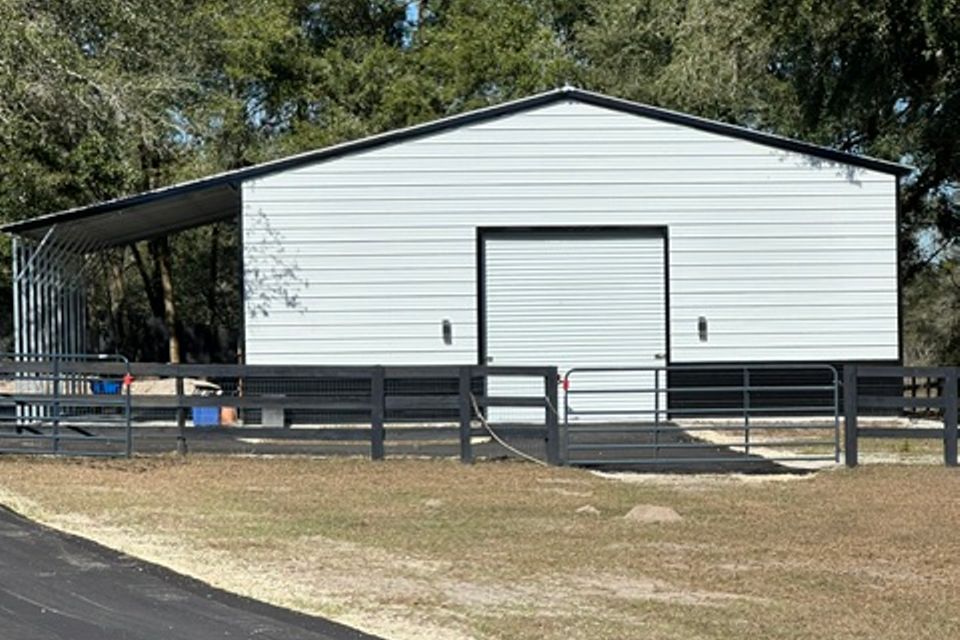 White steel barn with roll up door and side lean to on horse property representing steel barns in Alabama