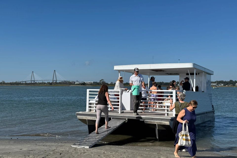 Guests stepping off the Roamer IV pontoon onto a Charleston harbor beach with the Ravenel Bridge in the background