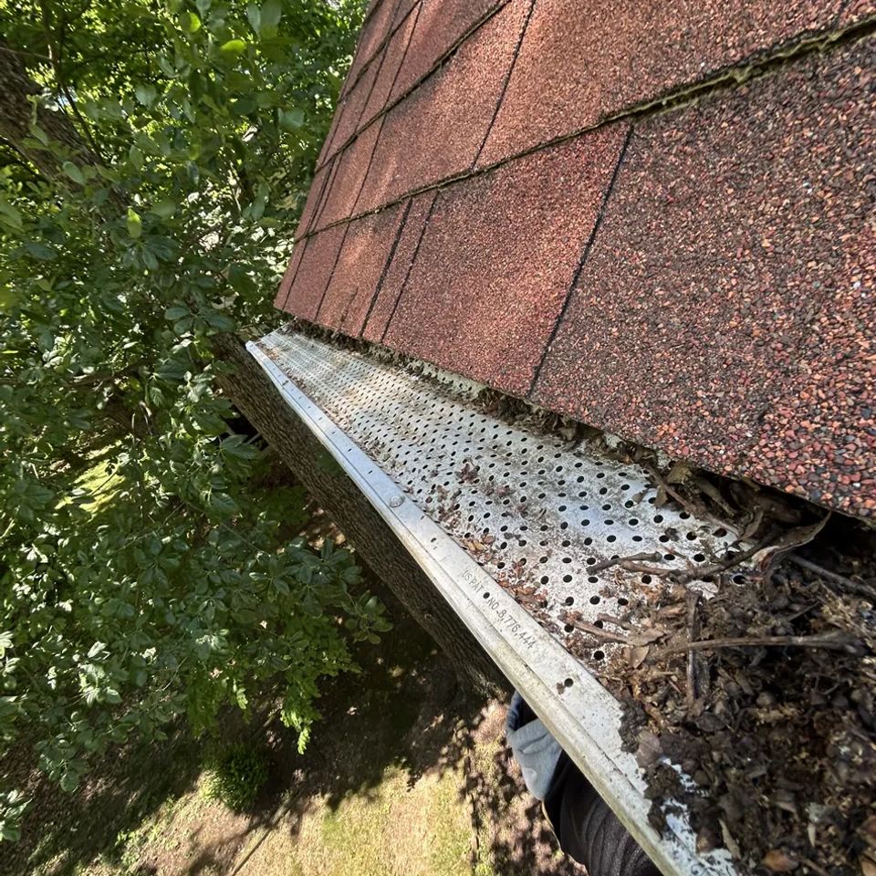 Debris-filled gutter with mesh guard along red shingle roof after gutter cleaning in Harrisburg PA