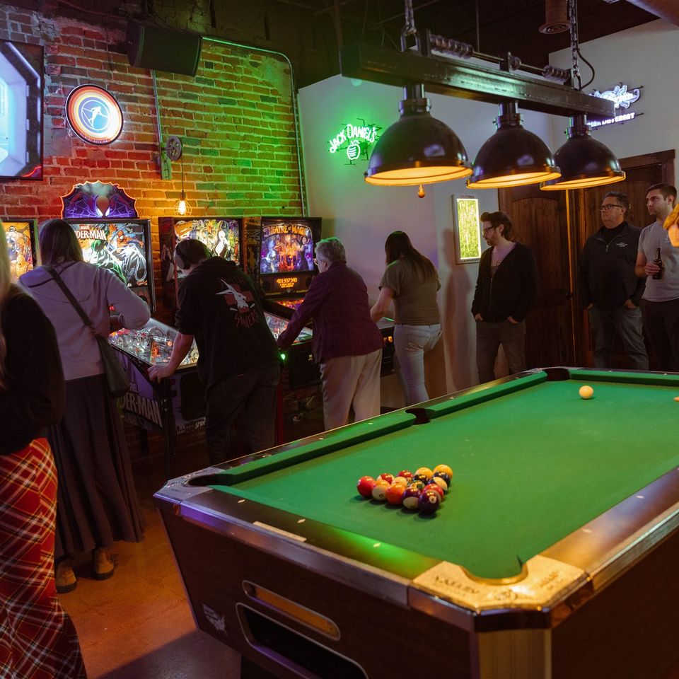 Group of people playing pinball machines and pool