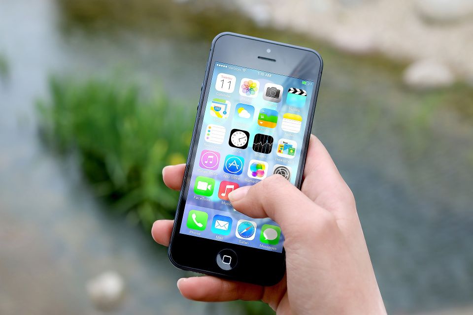 Hand holding iPhone, scrolling through apps.