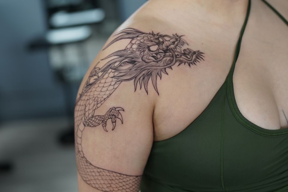 Image of a large angry dragon on a womans shoulder and wrapping around her arm down to her elbow