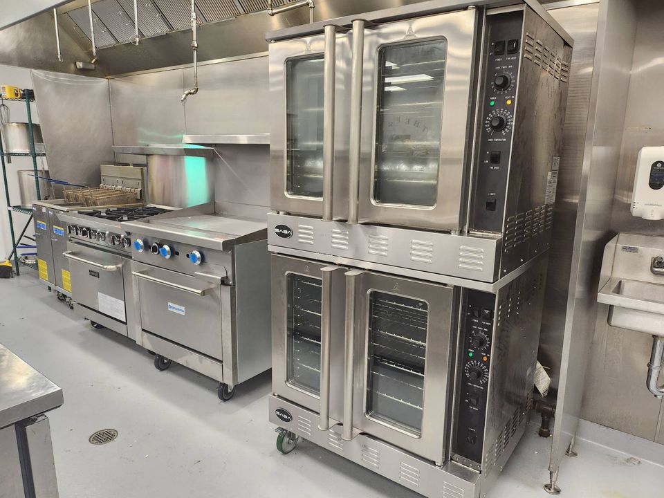 commercial restaurant kitchen line with double convection oven, flat top grill with oven, 6 burner range, deep fat fryers under hood ventilation system