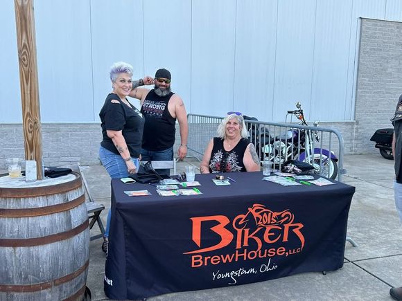 Event participants gathered around a vendor table during an outdoor biker community event.