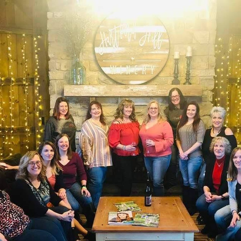 Group of women posing together in front of a fireplace decorated with warm string lights.