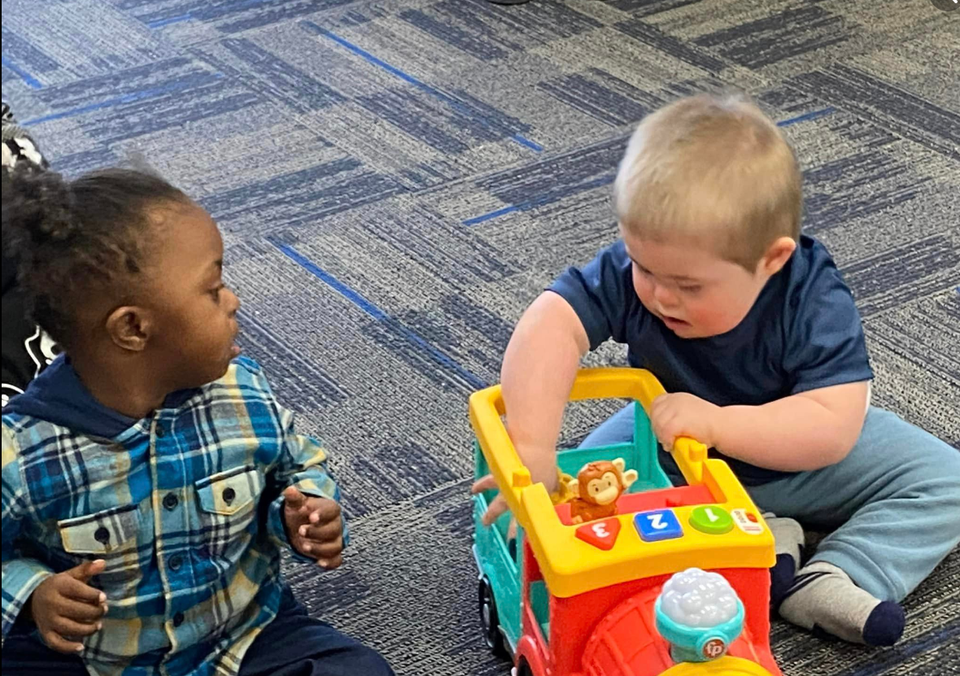 Two toddlers playing together with a colorful toy during a Down Syndrome Association of the Valley early childhood program.