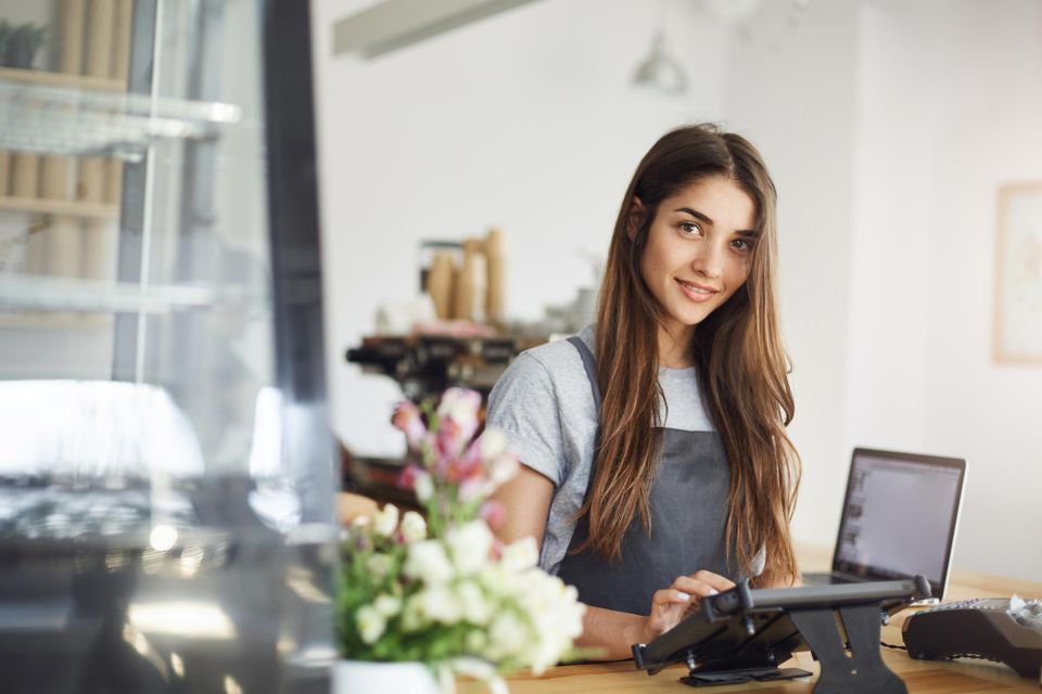 Coffee shop owner using tablet looking camera smiling waiting her first customer