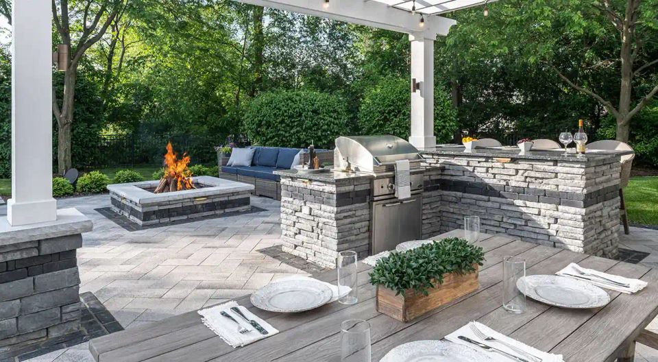 Luxury outdoor kitchen and fire pit patio with stone hardscape design and covered seating area in Charlotte NC