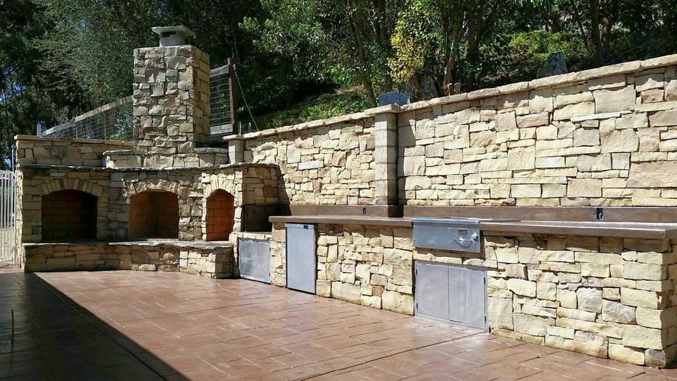Custom outdoor BBQ kitchen with stone veneer, built-in grill, and backyard entertainment area