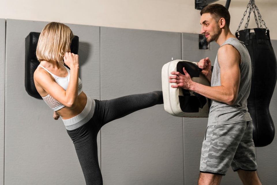 Woman throwing a high kick into a kick shield held by a coach during kickboxing training