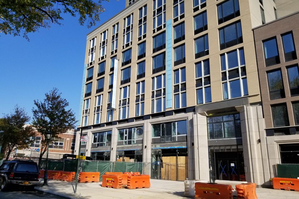 Tall vertical printed banner hanging down the facade of a new apartment building above a sidewalk lined with construction barriers