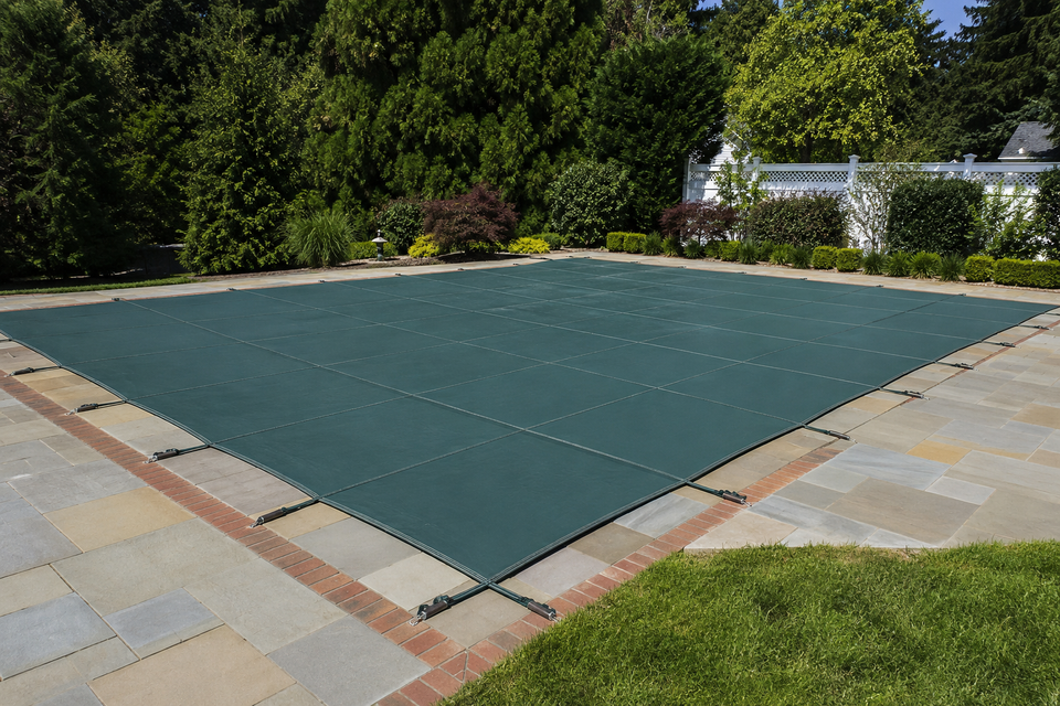 Green mesh safety cover installed over a rectangular inground pool on a bluestone patio in Long Island NY