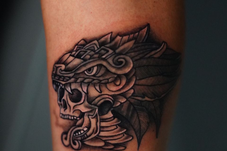 Image of a tattoo of a dragon consuming a skull in black and grey and a lot of intricate tattoo detail