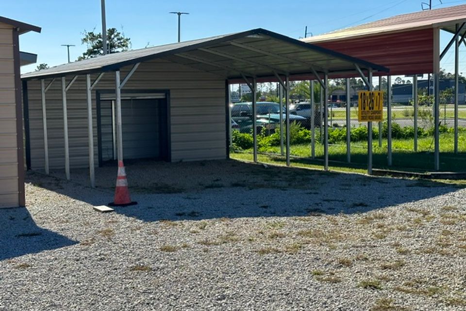 Tan steel garage with attached open carport bays and roll up door on gravel lot representing steel garages in Alabama