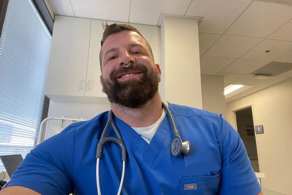 Smiling healthcare provider in blue scrubs with a stethoscope  seated in a bright exam room at be well berlin clinic.
