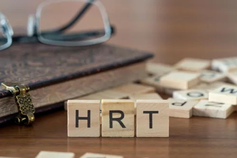 Scrabble tiles spelling hrt on a wooden desk  symbolizing hormone replacement therapy and gender affirming care.