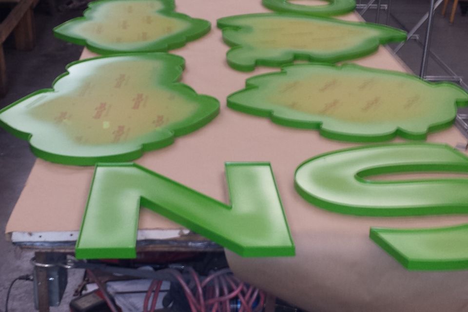 Green channel letters and logo faces laid out on the bench in the sign shop with awning frames racked behind