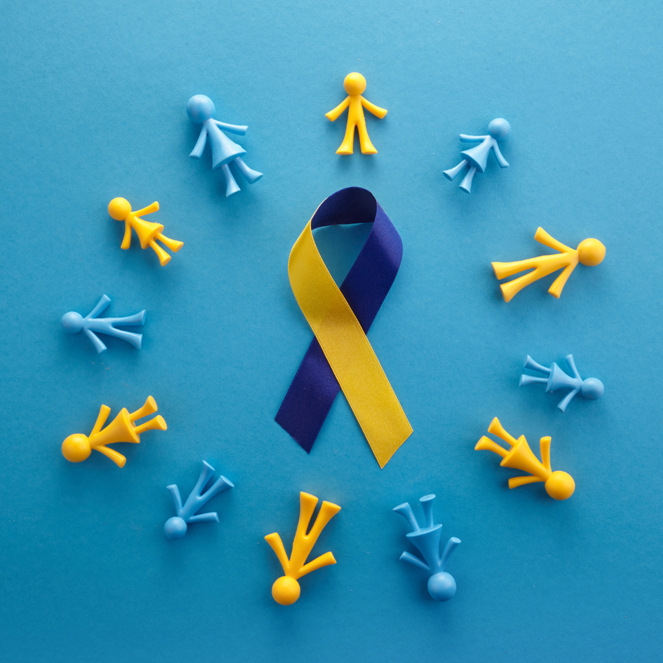 Blue and yellow Down syndrome awareness ribbon surrounded by blue and yellow figures on a blue background.