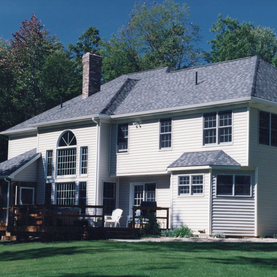 Rear view of a two-story custom home featuring a completed addition, large windows, a deck, and a spacious backyard.